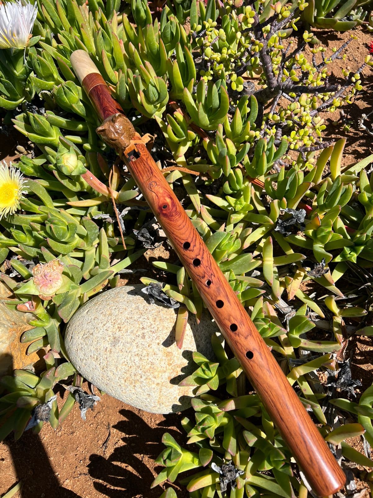 Rosewood flute with a carved bird totem, resting on succulents and a smooth stone