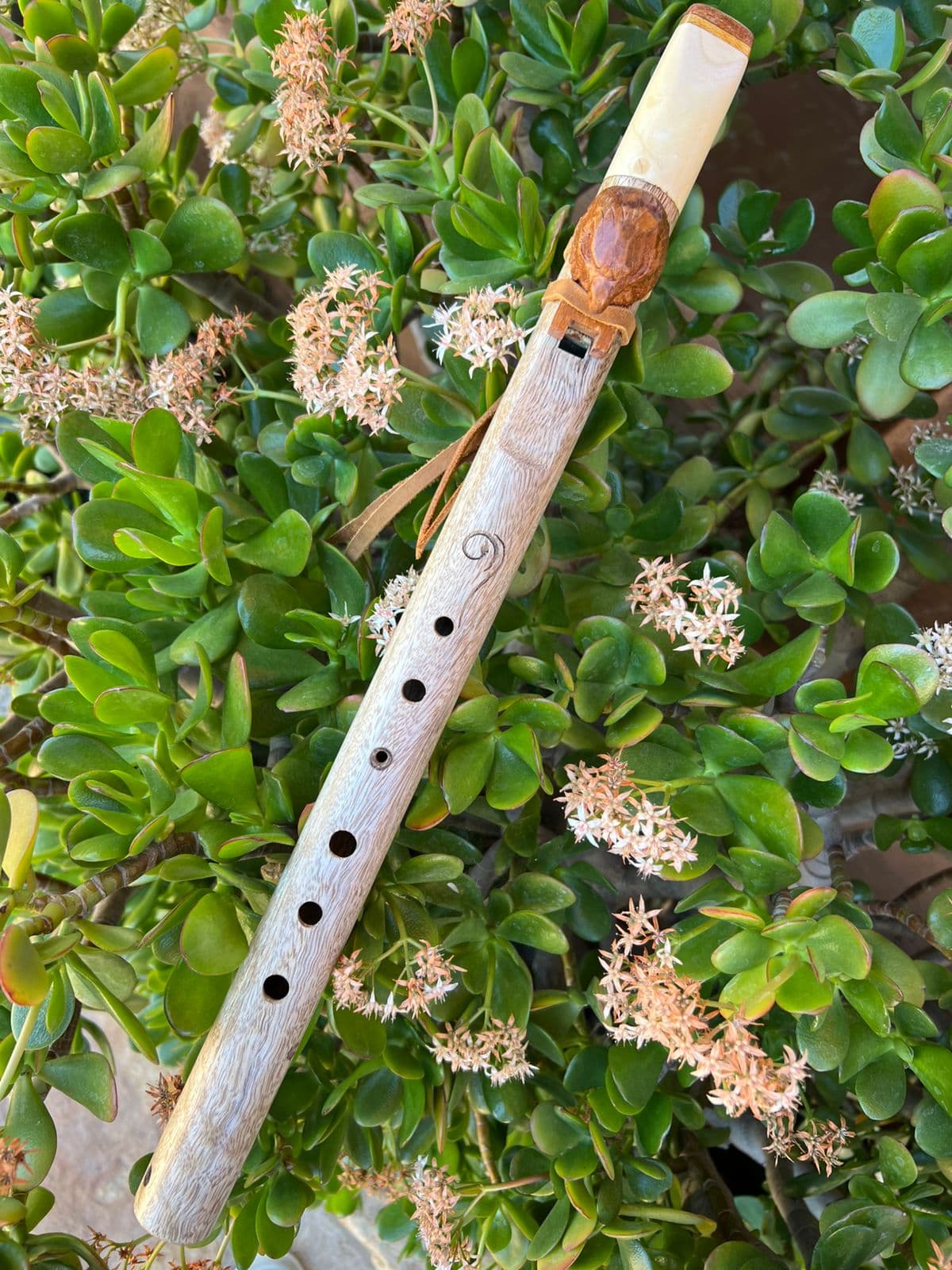 Pale birch flute with a spiral burn motif and a small bird totem, among white flowers
