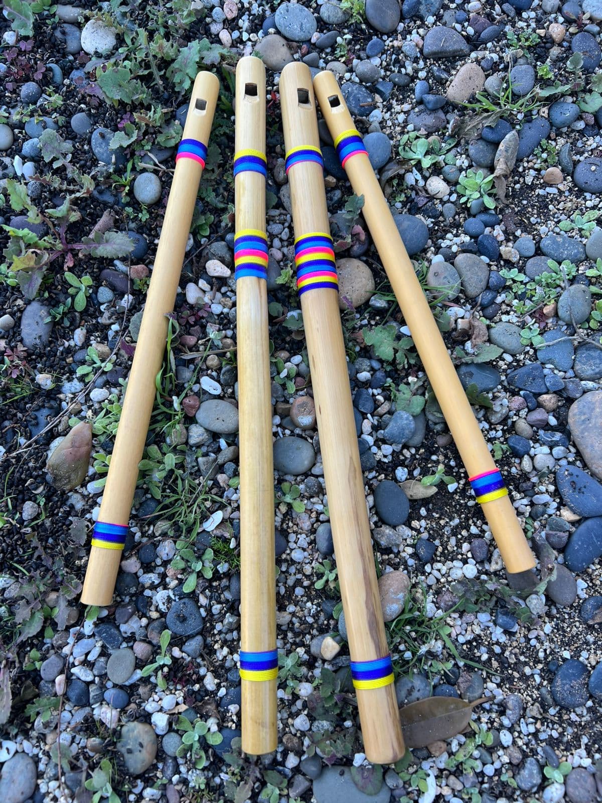 Golden bamboo flutes bound with bright waxed thread, resting on river stones