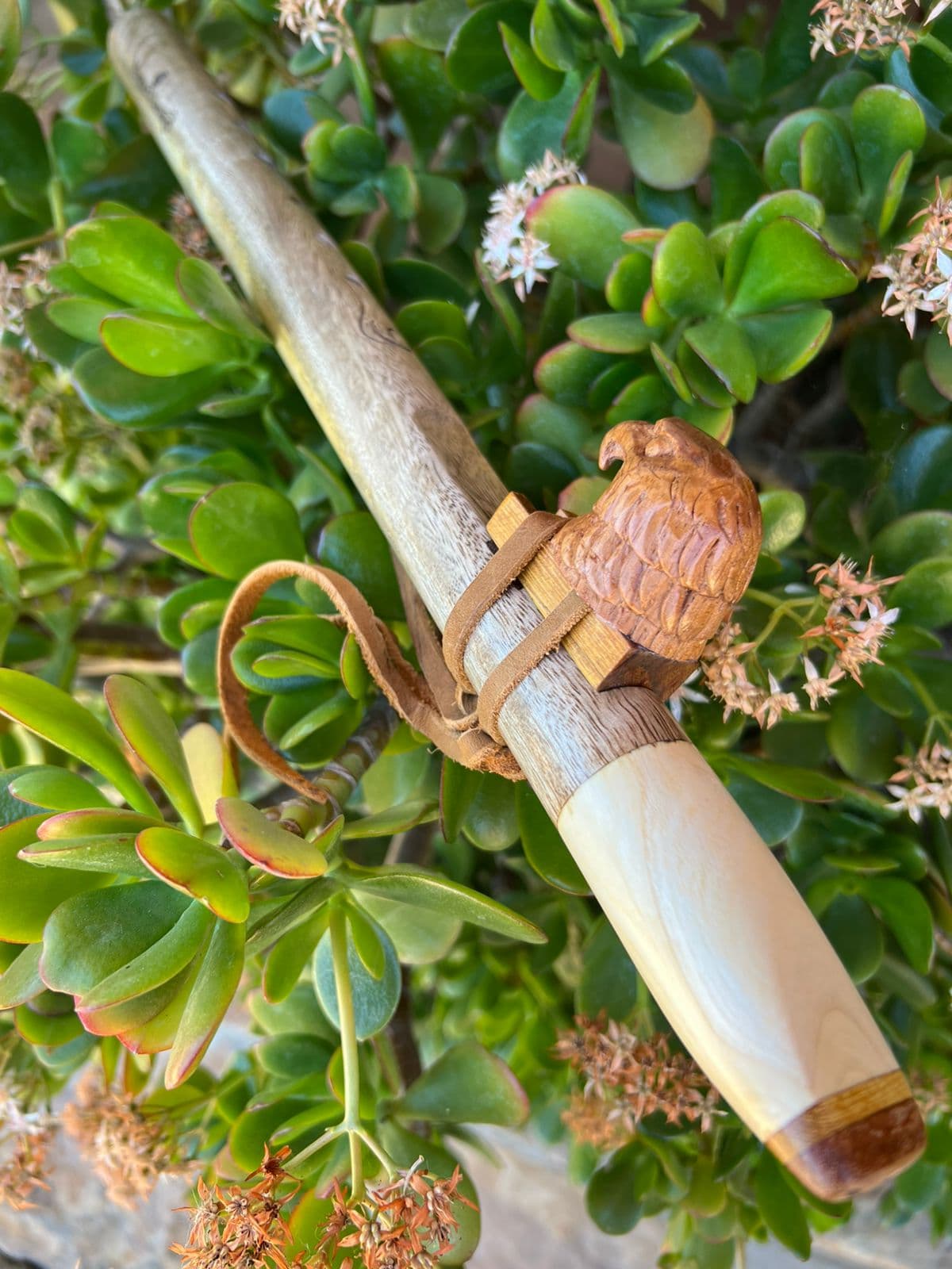 Pale maple flute with a carved eagle totem, on a flowering jade plant